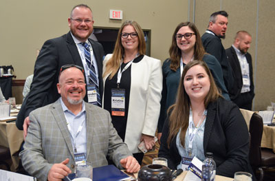 Photo of WHLA Board and Committee members at the 2019 Wisconsin Lodging Conference & Trade Show. Five people in the photo, all in business professional clothing (suit jackets & blazers). One man and one woman sitting at the table. One man and two women standing behind them.