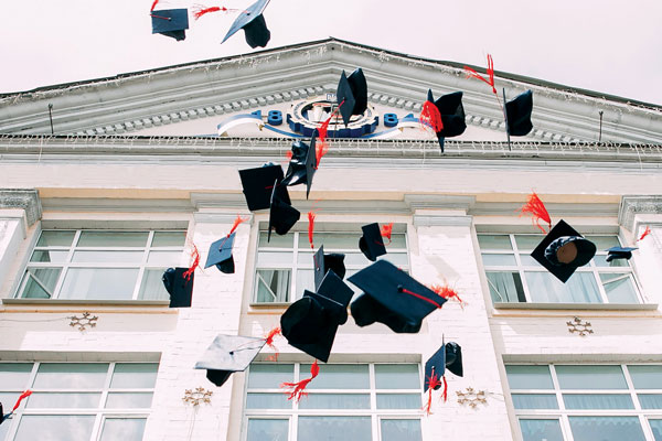 Graduation caps thrown in the air in from of an educational institution building