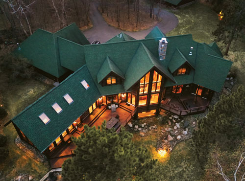 Aerial photo of a large lodge in the woods lit up at night with a green roof.