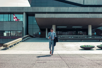 Image of a business man walking outside a large business building in a grey suit while on his phone.