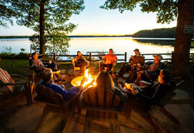 Pitlik's Sand Beach Resort (Eagle River, WI). Photo taken shortly after sunset of people sitting around campfire with lake in the background.